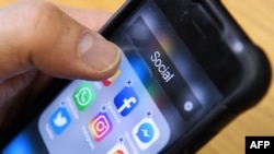 Seorang pria memegang ponsel pintar dengan ikon aplikasi jejaring sosial Facebook, Instagram dan Twitter terlihat di layar di Moskow pada 23 Maret 2018. (Foto: AFP)