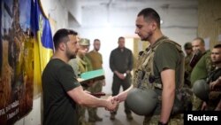 Presiden Ukraina Volodymyr Zelenskyy bersalaman dengan salah satu anggota pasukan Ukraina dalam kunjungannya ke garis depan pertempuran di Kota Pokrovsk, wilayah Donetsk, Ukraina, pada 26 Juni 2024. (Foto: Ukrainian Presidential Press Service/Handout via Reuters)