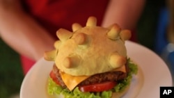 Pemilik restoran Hoang Tung memperlihatkan "burger corona" di Hanoi, Vietnam pada hari Rabu, 25 Maret 2020. Saat ini dunia sedang berjuang melawan pandemi Covid-19. (Foto: AP)
