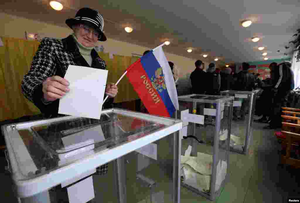 Seorang perempuan memegang bendera Rusia ketika memberikan suaranya dalam referendum status wilayah Krimea, Ukraina di sebuah tempat pemungutan suara di Bakhchisaray, Krimea, Ukraina, 16 Maret 2014.