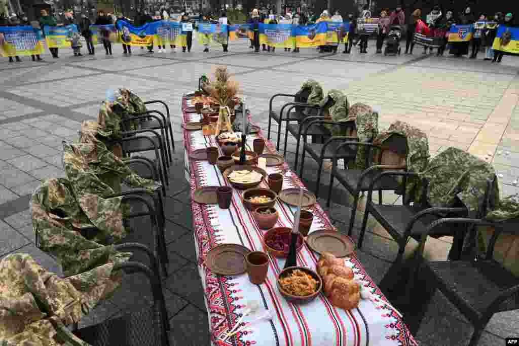 Soldiers' uniforms hang on empty chairs next to a symbolic Christmas table set with traditional dishes as people attend a rally in support of prisoners of war and missing soldiers in Lviv, Ukraine, Dec. 21, 2024.