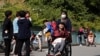 A woman pushes an elderly man in a wheelchair as residents play with their children near a commercial office building in Beijing on May 10, 2021.