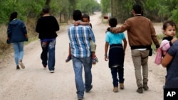 FILE - Migrant families walk from the Rio Grande, the river separating the U.S. and Mexico in Texas, near McAllen, Texas, right before being apprehended by U.S. Border Patrol, March 14, 2019.