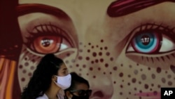 FILE - Women wear face masks as they wait at a COVID-19 testing site in the Estrutural neighborhood of Brasilia, Brazil, May 26, 2020.