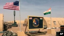 In this photo taken April 16, 2018, a U.S. and Niger flag are raised at the base camp for air forces and other personnel supporting the construction of Niger Air Base 201 in Agadez, Niger. On the edge of the Sahara Desert, the U.S. is building a base for armed drones.