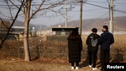 资料照:2021年2月12日,在韩国农历新年到来之际,一名脱北者和他的孩子们站在京畿道坡州市非军事区附近的铁丝网前。(路透社)