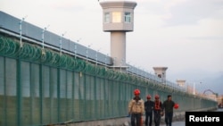 中国新疆维吾尔自治区达坂城的官方所谓的职业技能教育中心的围栏旁边，有工人走过。(2018年9月4日)