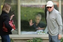 Judie Shape, center, who has tested positive for the coronavirus, but isn't showing symptoms, presses her hand against her window after a visit through the window and on the phone with her relatives, March 17, 2020, in Kirkland near Seattle.