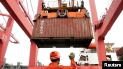 FILE - An employee guides as a crane unloads shipping containers from a cargo ship at a port in Lianyungang, Jiangsu province, China.