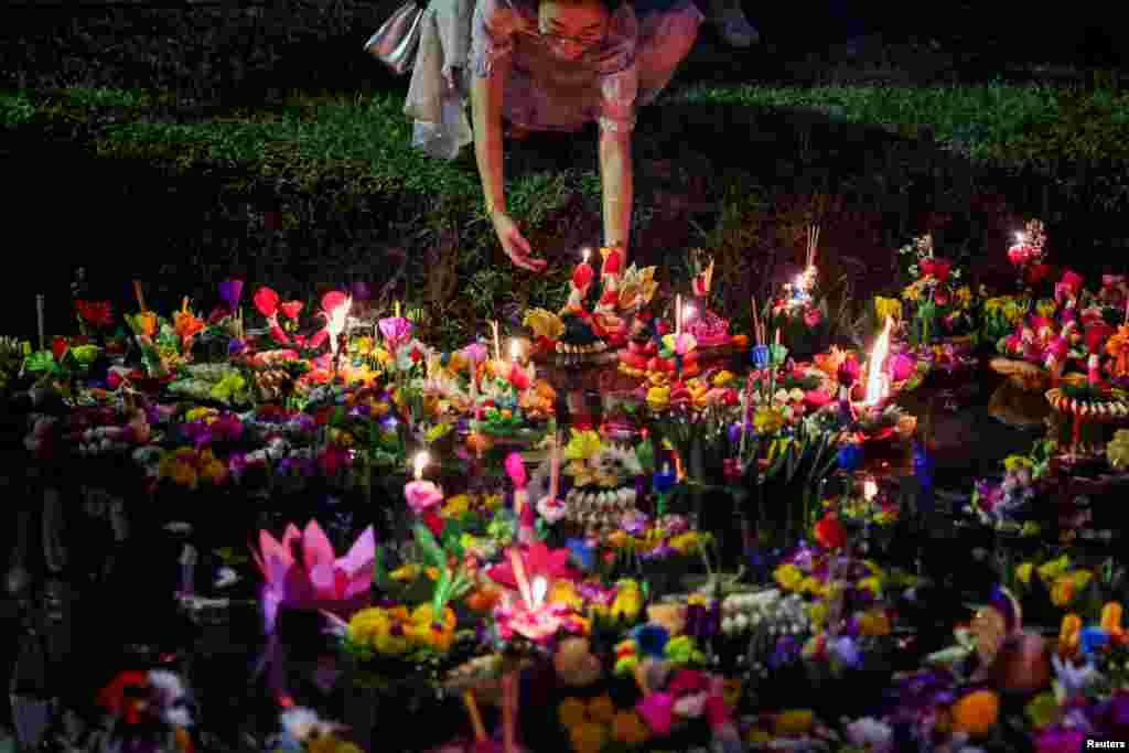 A woman places a Krathong, a floating basket made with leaves and flowers, into a park's lagoon during the Loy Krathong festival, a symbolic apology and expression of gratitude to the goddess of the river for the water, in Bangkok, Thailand.