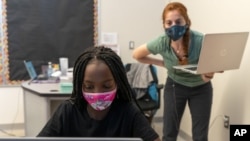In this Tuesday, Sept. 29, 2020, photo English Language Arts teacher Rebecca Ain, right, helps a student in her class at The Social Justice Public Charter School, in Washington. (AP Photo/Jacquelyn Martin)