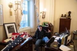 A supporter of President Donald Trump sits inside the office of Speaker of the House Nancy Pelosi inside the Capitol in Washington, Jan. 6, 2021.