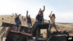  FILE - Protesters against the Dakota Access oil pipeline stand on a burned-out truck near Cannon Ball, N.D., that they removed from a long-closed bridge near their camp in North Dakota, Monday, Nov. 21, 2016. 