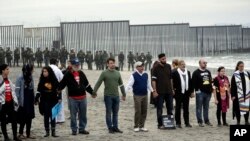 Orang-orang bergandengan tangan seraya berdoa saat berunjuk rasa di San Diego, dekat perbatasan dengan Tijuana, Meksiko, 10 Desember 2018 (foto: AP Photo/Gregory Bull)