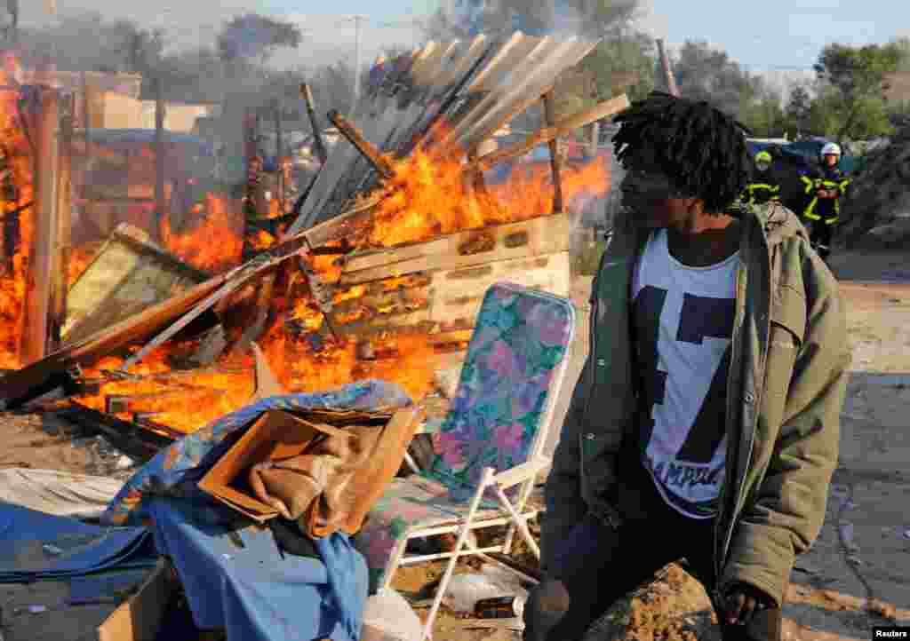 A migrant walks past a burning makeshift shelter set ablaze in protest against the dismantlement of the camp for migrants called "the jungle" in Calais on the second day of their evacuation and transfer to reception centers, France, Oct. 25, 2016.