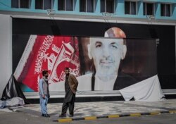 FILE - Afghan men stand next to a torn poster of Afghan President Ashraf Ghani at the Kabul airport in Kabul on August 16, 2021.