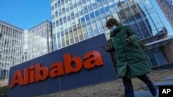 Seorang perempuan yang mengenakan masker berjalan melewati kantor perusahaan e-commerce asal China, Alibaba, di Beijing, pada 13 Desember 2021. (Foto: AP/Andy Wong)