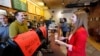 FILE - Molly Kepner, right, smiles after hearing the news of her discount from Tom Grover at The Works Bakery Café in Concord, N.H., April 12, 2016. The New Hampshire bakery chain gave women a break in honor of Equal Pay Day, charging them 79 percent of their bill. 