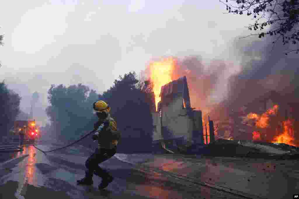 A firefighter battles the advancing Palisades Fire as it burns a structure in the Pacific Palisades neighborhood of Los Angeles, Jan. 7, 2025. 