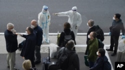 A worker in protective coverings directs members of the World Health Organization (WHO) team on their arrival at the airport in Wuhan in central China's Hubei province on Thursday, Jan. 14, 2021. A global team of researchers arrived Thursday in the…