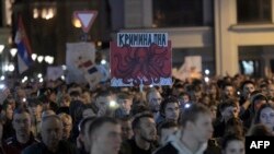 Seorang pedemo mengacungkan poster bertuliskan "kriminal" dalam demo pada Selasa, 28 Januari 2025, untuk menekan pemerintah atas insiden fatal runtuhnya atap stasiun kereta Novi Sad pada November tahun lalu. (Foto: Nenad Mihajlovic/AFP)