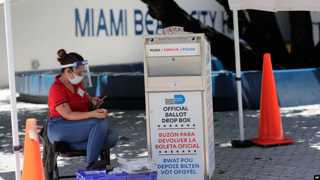FILE - A poll worker monitors a ballot drop box for mail-in ballots outside a polling station during early voting, Aug. 7, 2020, in Miami Beach, Fla.