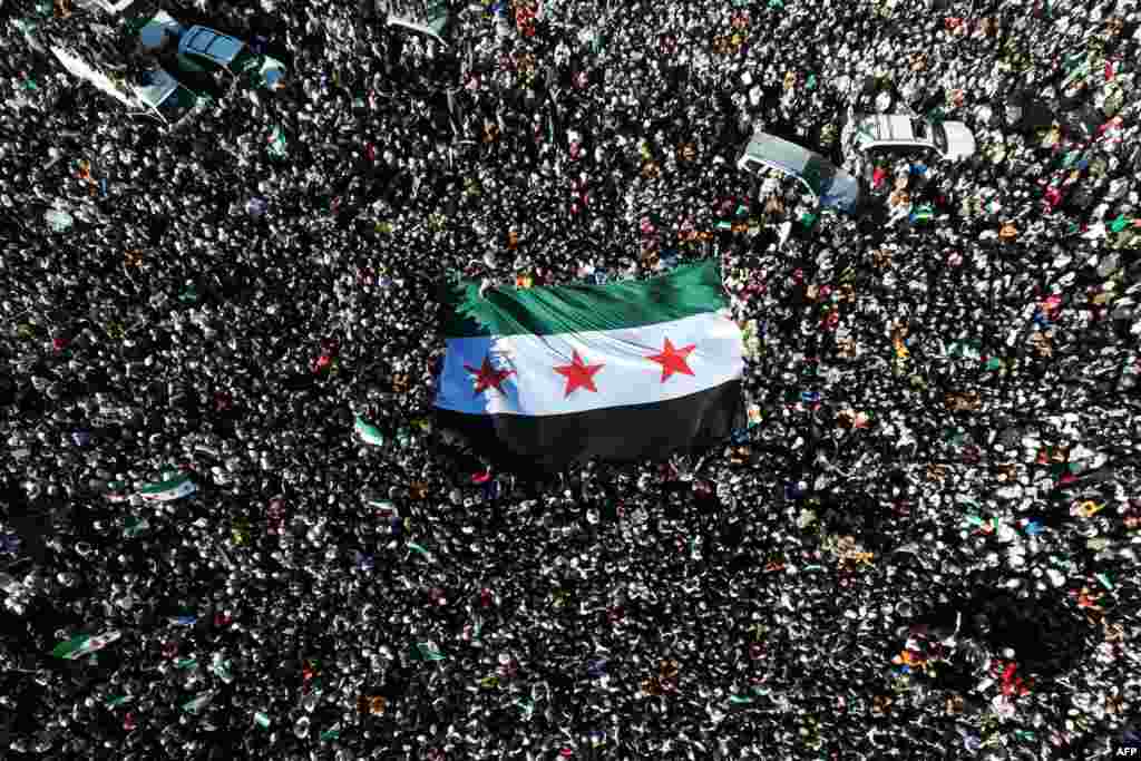 Crowds of Syrians raise a giant independence-era flag, used by the opposition since the uprising began in 2011, as they celebrate the fall of Bashar al-Assad's iron-fisted rule earlier this week, at the central Umayyad Square in Damascus.