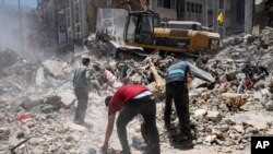 Peralatan konstruksi digunakan untuk menyaring puing-puing sebelum diangkut dari lokasi bangunan yang hancur dalam serangan udara sebelum gencatan senjata yang menghentikan perang 11 hari antara penguasa Hamas Gaza dan Israel, 27 Mei 2021, di Gaza Kota. (Foto: AP)