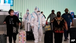 FILE - Air China flight crew members in hazmat suits walk through the arrivals area at Los Angeles International Airport in Los Angeles, Nov. 30, 2021.