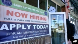 FILE - A man walks into a restaurant displaying a "Now Hiring" sign, in Salem, New Hampshire, March 4, 2021.