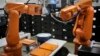 File - A Chinese worker is seen behind orange robot arms at work at Rapoo Technology factory in southern Chinese industrial boomtown of Shenzhen, Aug. 21, 2015.