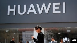 Para pejalan kaki berjalan melewati toko retail Huawei di Beijing, 30 Juni 2019. (AP Photo)