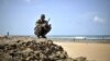 A handout picture released by the African Union-United Nations Information Support Team shows an armed man squatting at a beach during a demonstration by a local militia, formed in order to provide security in the town of Marka, April 30, 2014.