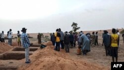 FILE - Officials and residents stand near freshly dug graves on June 11, 2019, in a Dogon village in Mali after an attack on ethnic Dogon on June 9, 2019. 