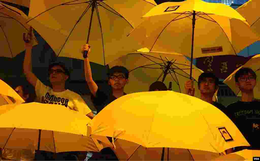 Joshua Wong (center left) and Alex Chow as they join other Umbrella Movement leaders unfurling umbrellas at the rally marking the one-month point since the beginning of the protests in Hong Kong (Ivan Broadhead/VOA).