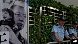 Polisi berdiri di samping potret peraih Nobel Perdamaian China Liu Xiaobo saat berlangsungnya aksi unjuk rasa di luar kantor penghubung China di Hong Kong, 10 Juli 2017.