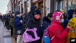 Seorang pria tampak membawa kursi plastik saat mengantre untuk membeli suvenir Olimpiade Musim Dingin Beijing di salah satu toko di Beijing, pada 7 Februari 2022. (Foto: AP/Andy Wong)