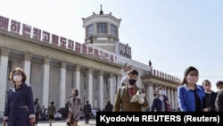 마스크를 쓴 북한 평양 시민들이 김정은 국무위원장 찬양 문구가 적힌 평양역 앞에서 이동하고 있다. (자료사진)