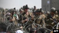 Tentara AS berjaga di balik kawat berduri saat warga Afghanistan duduk di pinggir jalan dekat bagian militer bandara di Kabul, 20 Agustus 2021.(Foto: AFP)
