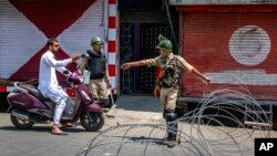 Tentara paramiliter India menanyai seseorang dengan motor sebelum membiarkan dia melewati sebuah pos pemeriksaan kawat berduri yang didirikan oleh pasukan keamanan India di Srinagar, Kashmir yang dikuasai India, 7 Juli 2017.