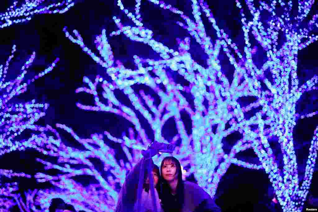 Visitors take selfie photos under Zelkova trees, lit up with blue LEDs during an illumination event called "Ao no Dokutsu," or Blue Cave, to celebrate the Christmas season at Shibuya district in Tokyo, Japan.