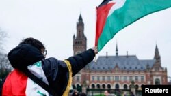 Seorang pria mengibarkan bendera Palestina ketika massa melakukan demonstrasi pada hari sidang publik yang diadakan oleh Mahkamah Internasional (ICJ) di Den Haag, Belanda, 21 Februari 2024. (Foto: Reuters)