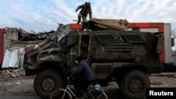 Seorang pria mengendarai sepeda melewati tentara yang berada di atas kendaraan militer di sebuah jalan di Lyman, Donestk, Ukraina, pada 11 Desember 2022, di tengah serangan pasukan Rusia yang terus berlangsung di Ukraina. (Foto: Reuters/Shannon Stapleton)