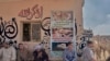 Camel herders at the market sit below a poster warning against mistreatment of the animals. Some of the vendors, in response to growing criticism on social media, insist not all herders and sellers are the same. (VOA/H. Elrasam)