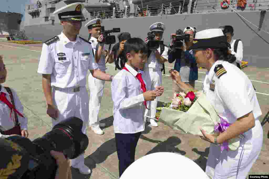 美军斯泰雷特号导弹驱逐舰2017年6月12日抵达中国湛江港时女舰长卡洛里从中国少年手里接过鲜花后,展示该军舰的纪念性硬币(美国海军照片)。 这是特朗普行政当局年初上任以来两国海军之间首次进行舰艇互访,这标志着美中两国恢复了搁置几个月之久的海军互访项目。