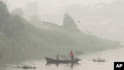 Warga mendayung perahu di Sungai Siak yang diselimuti kabut asap akibat kebakaran hutan di Pekanbaru, Riau (Oktober 2015). 