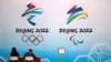FILE - Staff members sit near a board with signs of the 2022 Olympic Winter Games, at the National Aquatics Center in Beijing, China, April 1, 2021.