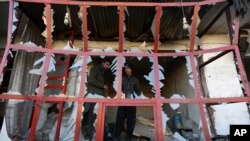 阿富汗一家商店在自杀爆炸手袭击附近卡车时遭到破坏， 从完全破损的橱窗玻璃可以看到店主正在审视店铺的损失。2015年12月28日（星期一）