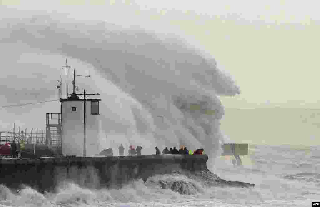 People watch as waves crash against the sea wall at Porthcawl, south Wales, as Storm Eunice brings high winds across the country.
