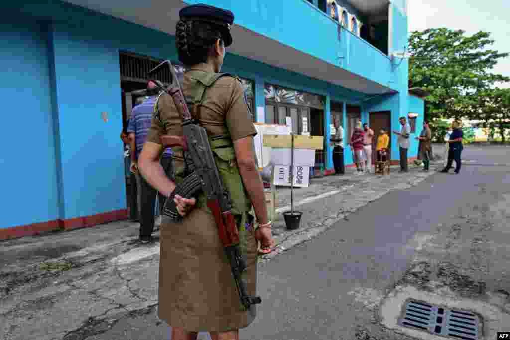 A policewoman keeps watch at a polling station as people queue before casting their ballots to vote in Sri Lanka's parliamentary election in Colombo.